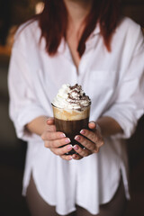 Coffee with whipped cream and chocolate chips in the hands of a girl