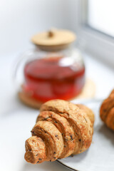 sweet healthy croissants decorated with seeds lie on a wooden kitchen round board on a white background next to a transparent teapot with a wooden lid. for splash screen banners banners in bacale