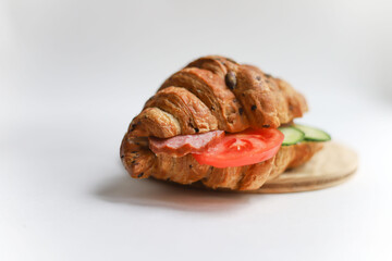 sweet healthy croissants garnished with seeds, sausage, tomato and cucumber lie on a wooden kitchen round board on a white background next to a transparent teapot with a wooden lid. for splash screen 