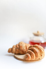 sweet healthy croissants decorated with seeds lie on a wooden kitchen round board on a white background next to a transparent teapot with a wooden lid. for splash screen banners banners in bacale