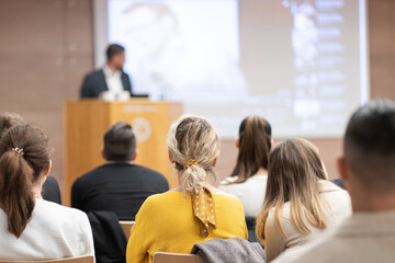 Fototapeta premium Speaker giving a talk in conference hall at business event. Rear view of unrecognizable people in audience at the conference hall. Business and entrepreneurship concept.