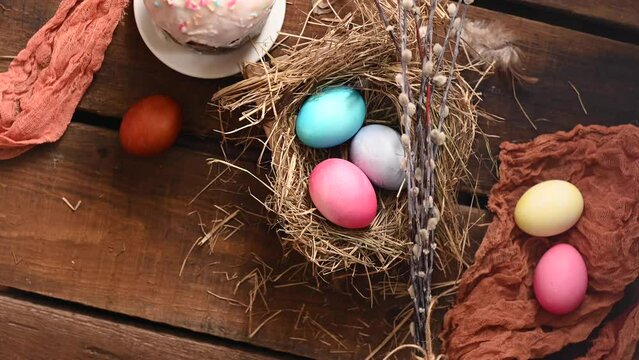 Easter is still life. Painted colorful chicken eggs in a hay nest, willow branches and fabric on a wooden table. Gyration. High quality 4k footage