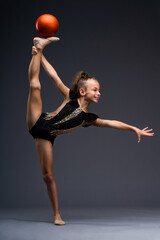 A little gymnast in a performance costume does acrobatic exercises with a ball. The girl wants to win