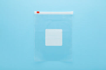 Empty transparent plastic zipper bag for freezer or food storage. Light blue table background. Pastel color. Closeup. Empty place for text on white label. Top down view.
