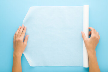 Young adult woman hands holding white roll of baking paper on light blue table background. Pastel...
