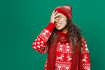 Young woman wear red warm cozy knitted sweater hat posing put hand on face facepalm epic fail mistaken omg gesture isolated on plain dark green color background. Happy New Year 2023 holiday concept.