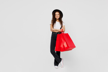 Full body smiling young woman wear t-shirt hat hold in hand red paper package bags after shopping hold hands crossed folded isolated on plain solid white background. Black Friday sale buy day concept.