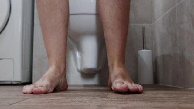 A man goes to the toilet in the toilet, takes off his denim shorts and begins the process of defecation. Healthy digestive tract and intestines.