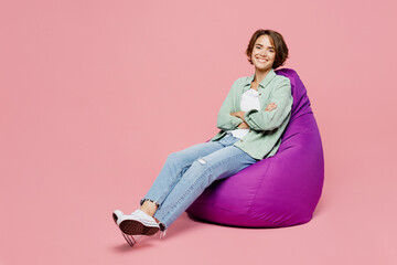 Full body young smiling happy fun woman 20s she wears green shirt white t-shirt sit in bag chair look camera isolated on plain pastel light pink background studio portrait. People lifestyle concept - Powered by Adobe