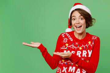 Merry surprised young woman wear xmas sweater Santa hat posing pointing hands arms aside indicate...