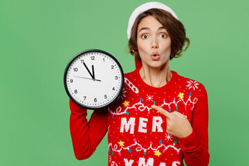 Merry young woman wear knitted xmas sweater Santa hat posing point index finger on clock show five...