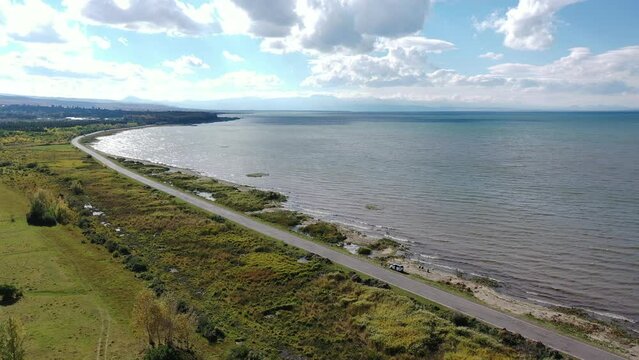 Highway traffic near water.  Road near Sevan lake in Armenia, Caucasus.  Aerial footage road between lake and field. Most popular lake in Armenia. Green field and lake with  blue sky background. 