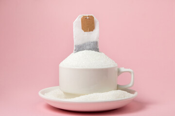 Tea with a lot of added sugar. Cup overflowing with sugar and tea bag on pink background