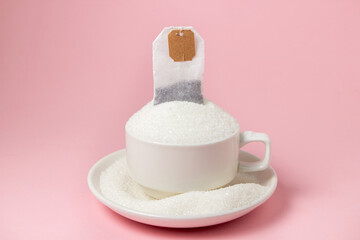 Tea with a lot of added sugar. Cup overflowing with sugar and tea bag on pink background