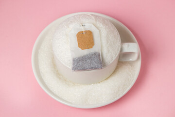 Tea with a lot of added sugar. Cup overflowing with sugar and tea bag on pink background