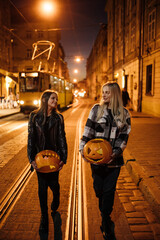 a mother with a teenage daughter walks through the evening city with Halloween pumpkins