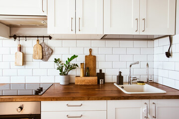 Fototapeta na wymiar Kitchen brass utensils, chef accessories. Hanging kitchen with white tiles wall and wood tabletop.Green plant on kitchen background 