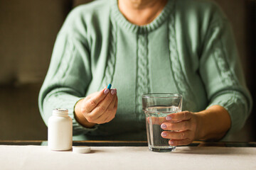 Woman's hands holds a blue capsule and glass of water over the table, ready to take medicines. Health care concept. 