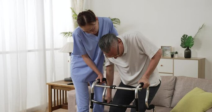 slow motion of asian older male stroke patient practicing using a walker with the assistance of his personal care attendant in the living room at home