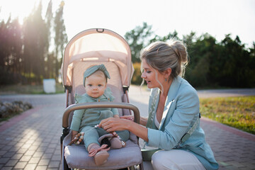 Young beautiful mother walks in the park with a child in a stroller. The mother leaned over to the...