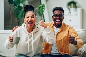 Multiracial couple watching television together at home on the couch