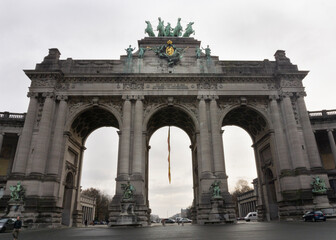 Fototapeta na wymiar Cinquantenaire Park Arc with quadriga bronze sculpture at the top of the scructure with belgium flag and cloudy sky at background 