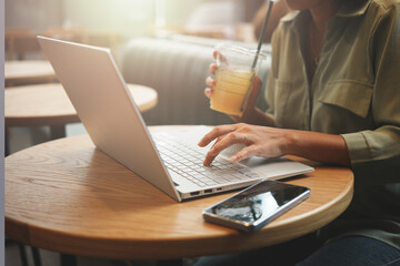 Woman working with laptop and drinking orange juice at cafe.