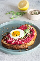 Whole grain toast with beetroot hummus, seeds, egg and microgreens (sprouted pea sprouts) on a light gray background. The concept of healthy eating..