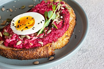 Whole grain toast with beetroot hummus, seeds, egg and microgreens (sprouted pea sprouts) on a light gray background. The concept of healthy eating..