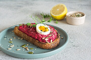 Whole grain toast with beetroot hummus, seeds, egg and microgreens (sprouted pea sprouts) on a light gray background. The concept of healthy eating..