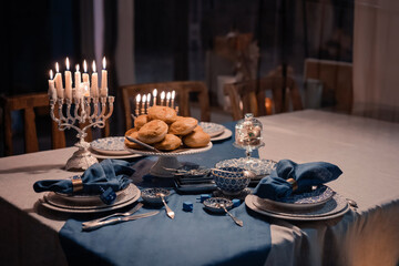 Food for Hanukkah celebration: Menorah Candles on wooden table, sufganiyot cake and table setting,...