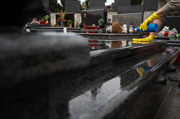 Headstone cleaning on cemetery. Professional in yellow gloves cleans the marble grave, polishing marble tombstone with special liquid,  preparation for All Saints Day on November 1st