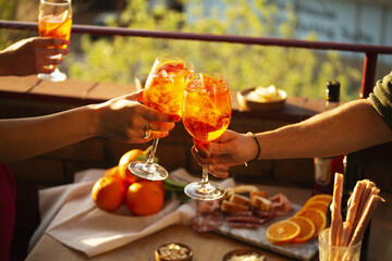 Two hands with glasses of Aperol Spritz cocktail in the sunset summer