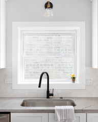 A beautiful kitchen sink detail with white cabinets, marble countertops, a hexagon tiled...