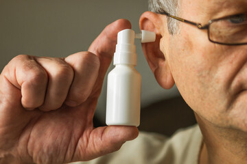 Caucasian senior man uses an ear spray. Man's hand holds a white ear spray bottle with nozzle...