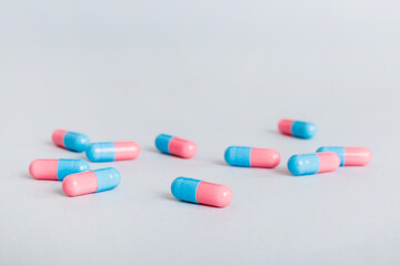 Heap of pink and blue pills on colored background. Tablets scattered on a table. Pile of red soft gelatin capsule. Vitamins and dietary supplements concept
