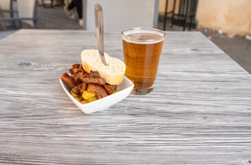 Close-up photo of a fresh beer in a glass and an aperitif of a serving of pork cheeks.