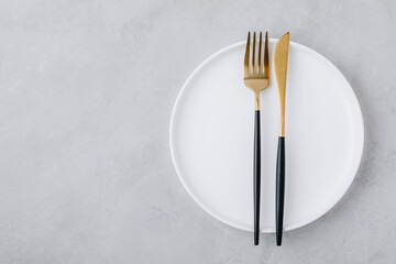 White empty plate with gold fork and knife on gray stone background, top view