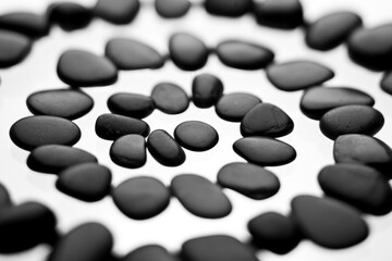 A spiral of small black stones on a white background with shallow focus.