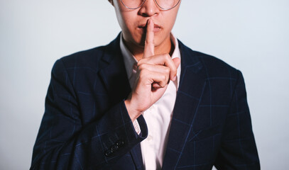 Photo closeup of Business man wearing classic costume looking on camera and holding index finger on lips isolated over white background.