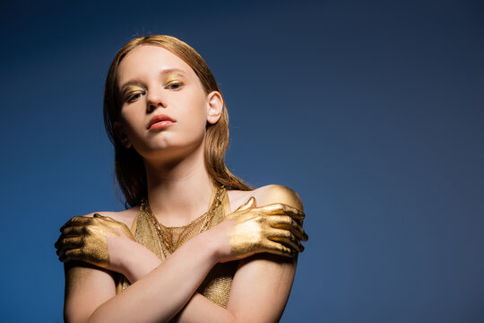 Pretty model with makeup and golden paint on hands looking at camera isolated on blue