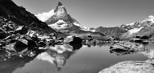 Matterhorn mountain panorama. Famous iconic peak near Zermatt in Wallis Switzerland in the Alps. Beautiful reflection in the “Riffelsee“ at Gornergrat Railway track. Black and white vintage pano. - obrazy, fototapety, plakaty