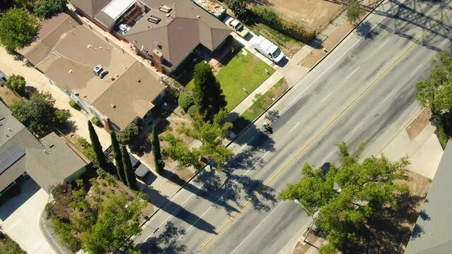 Aerial Shot Of Person Bicycling On Road In City, Drone Flying Backwards During Sunny Day - Los Angeles, California