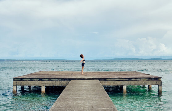 Female in Mountain pose on shabby wooden pier in sea