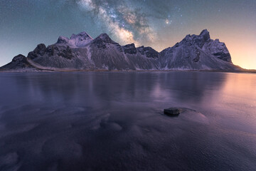 Snowy mountains near frozen lake under milky way sky