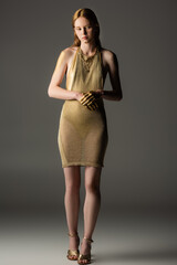 Full length of young woman in golden dress and paint looking away on grey background