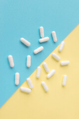 White pills on a yellow and blue pastel background. Capsules pills close-up. health care and medicine.	