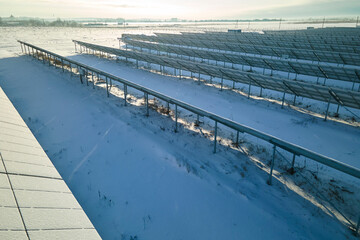 Aerial view of snow covered sustainable electric power plant with rows of solar photovoltaic panels for producing clean electrical energy. Low effectivity of renewable electricity in northern winter