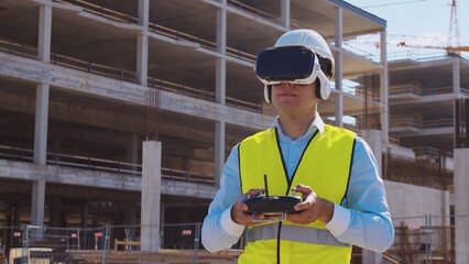 Professional drone operator in virtual reality helmet standing in front of construction site....
