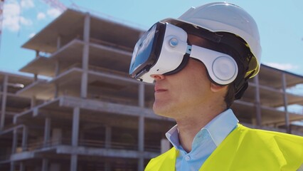 Professional builder in VR helmet standing in front of construction site and using virtual and...